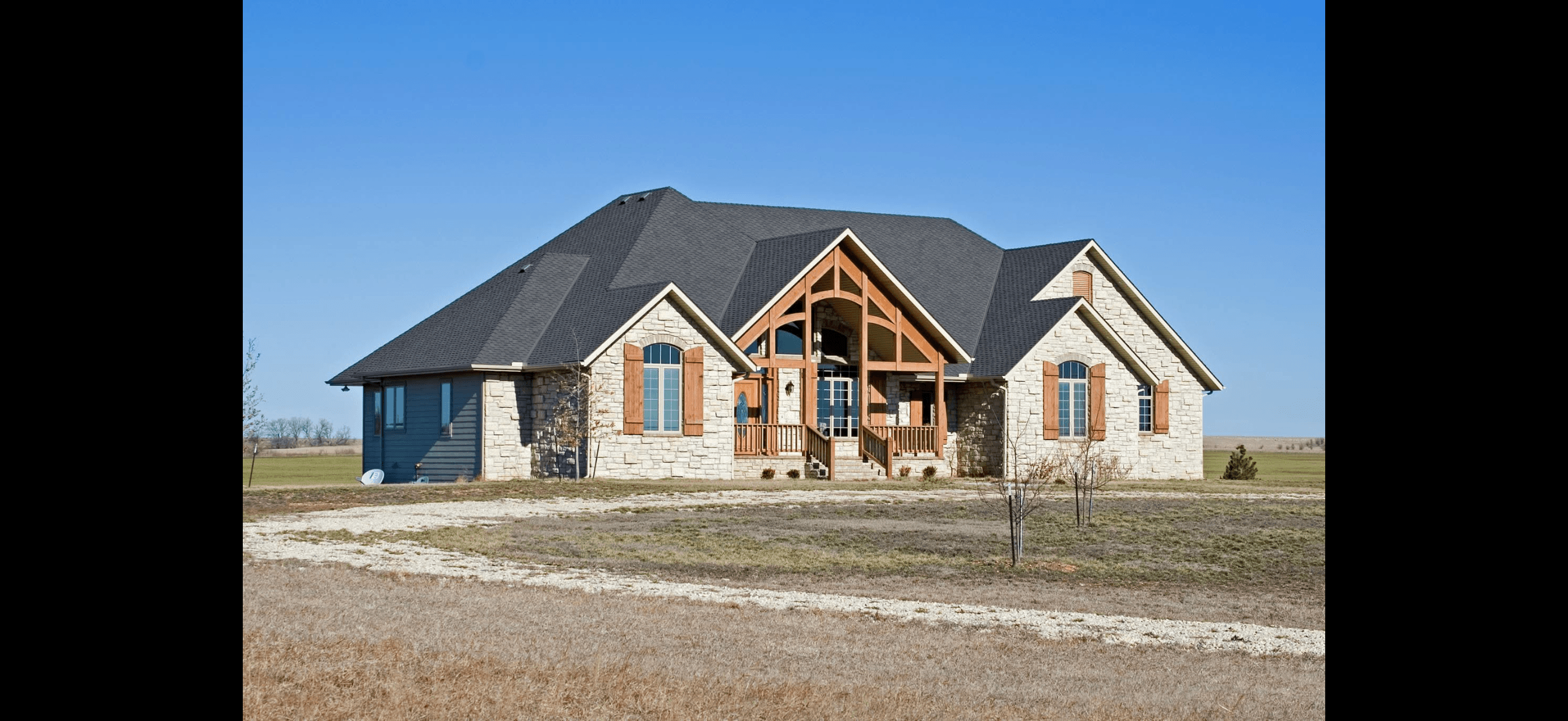 Large stone house featuring a timber-frame entrance and arched windows under a bright blue sky.