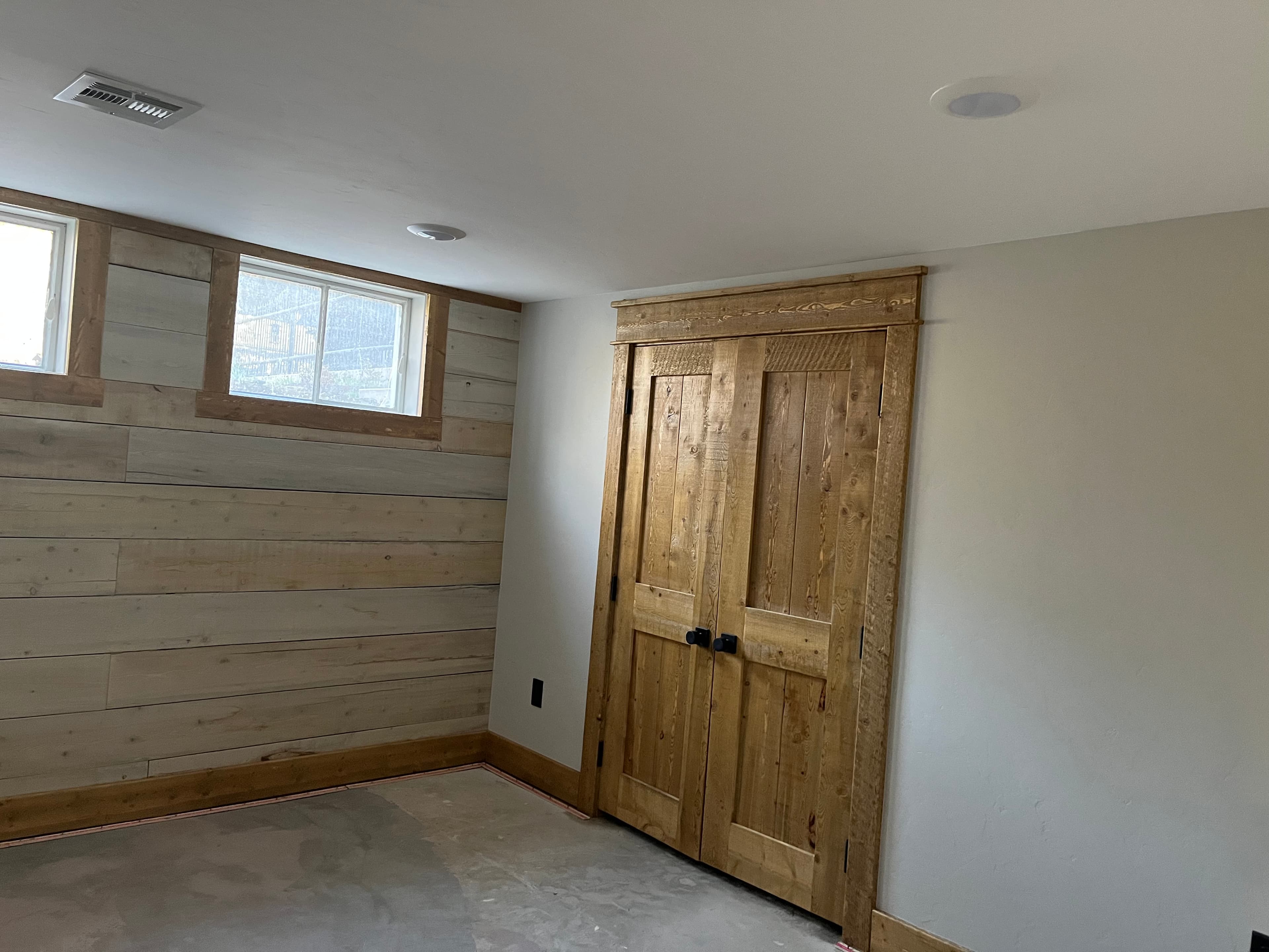 Double wooden doors and a wood-planked wall with a small window in an unfinished basement.