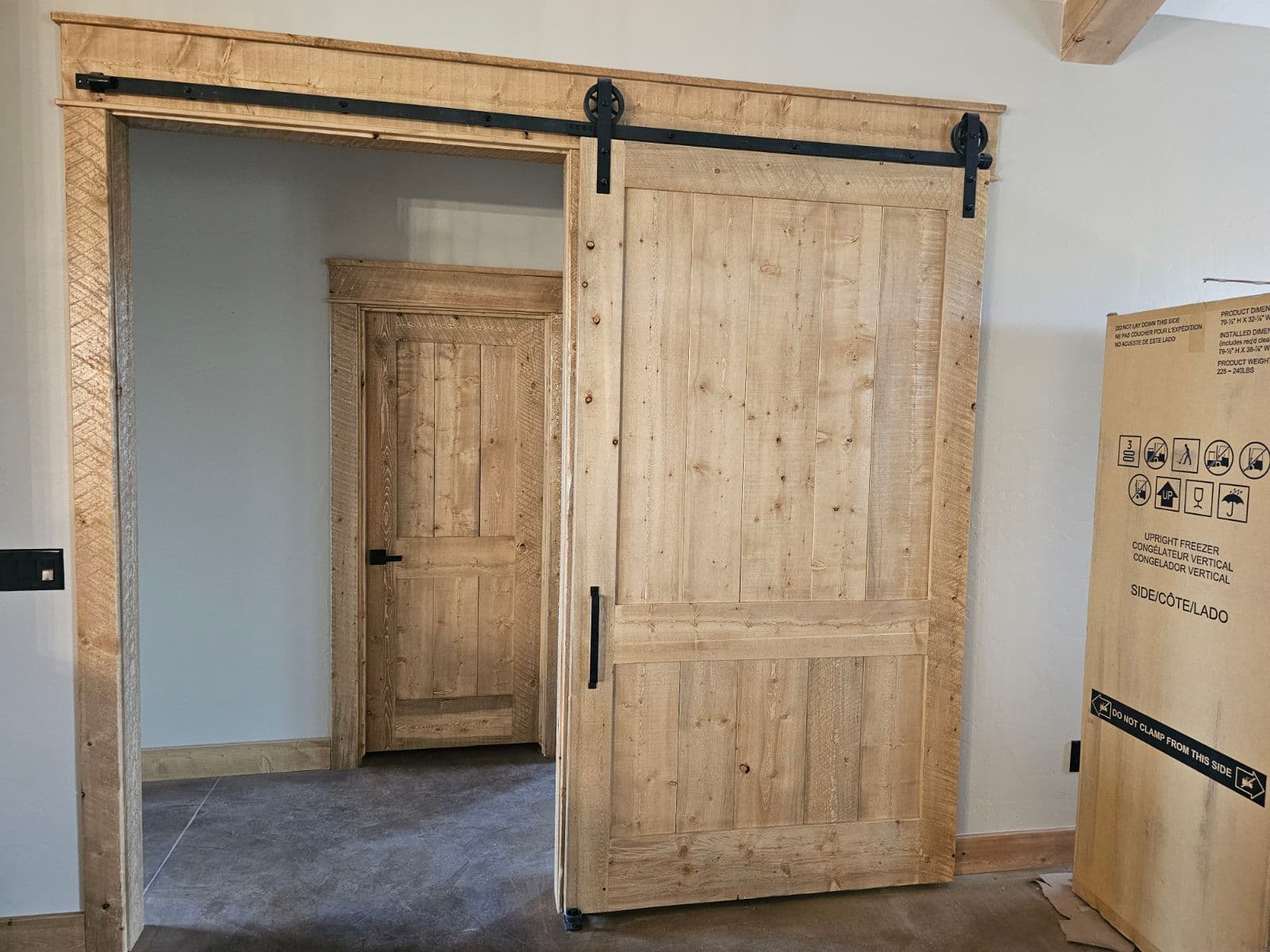 Rustic light wood sliding barn door partially open, revealing a matching door inside.
